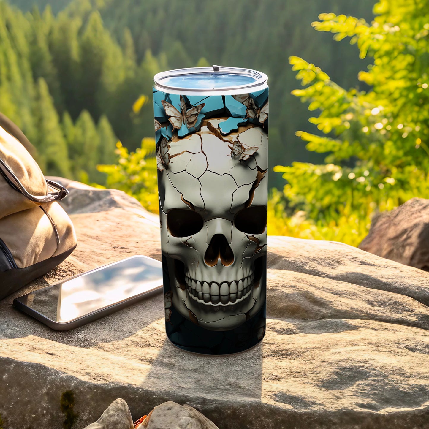 Tumbler with skull and butterfly design on a rock with mountains in background.