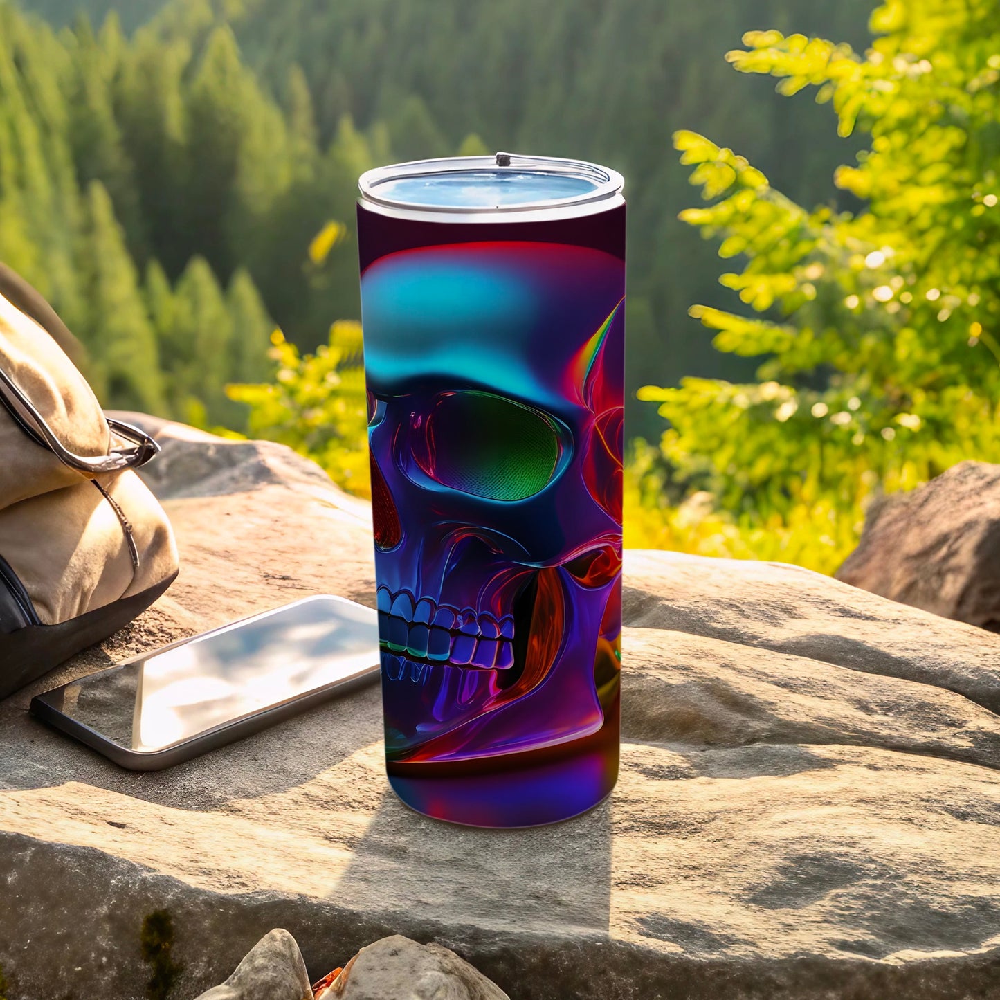 Gradient skull tumbler on a rock with backpack and phone outdoors.
