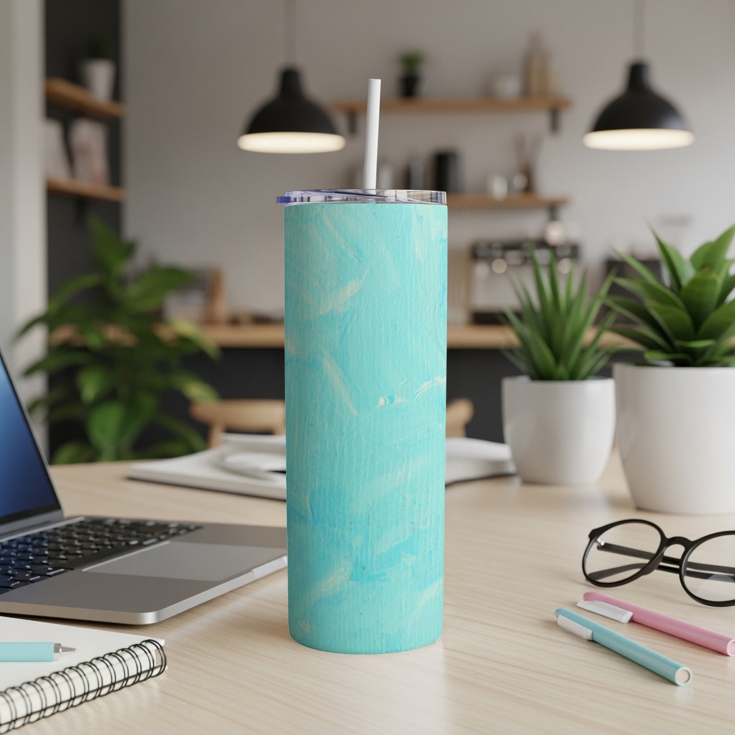 Teal and white marbled tumbler with straw on desk with laptop.