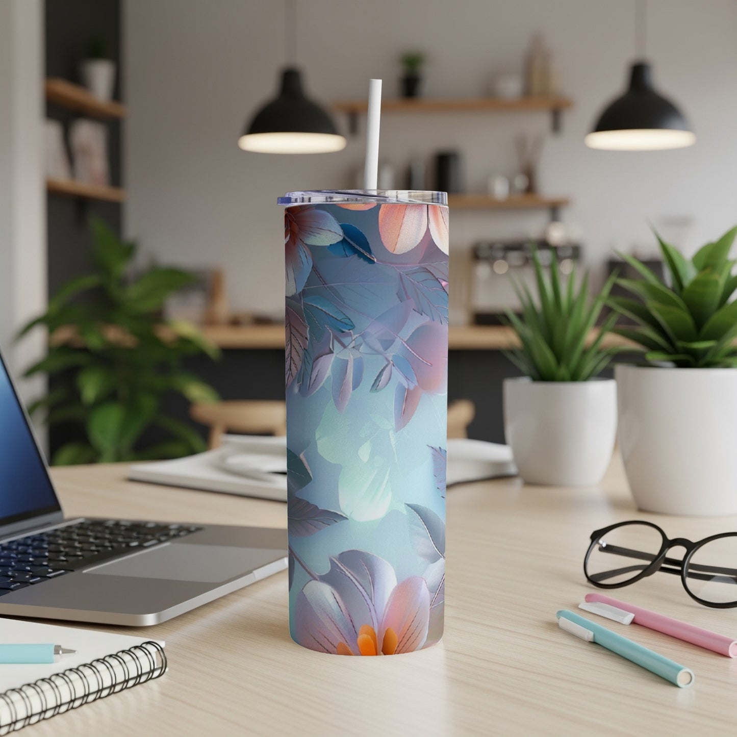 Floral design tumbler with straw on a desk with a laptop and pens.