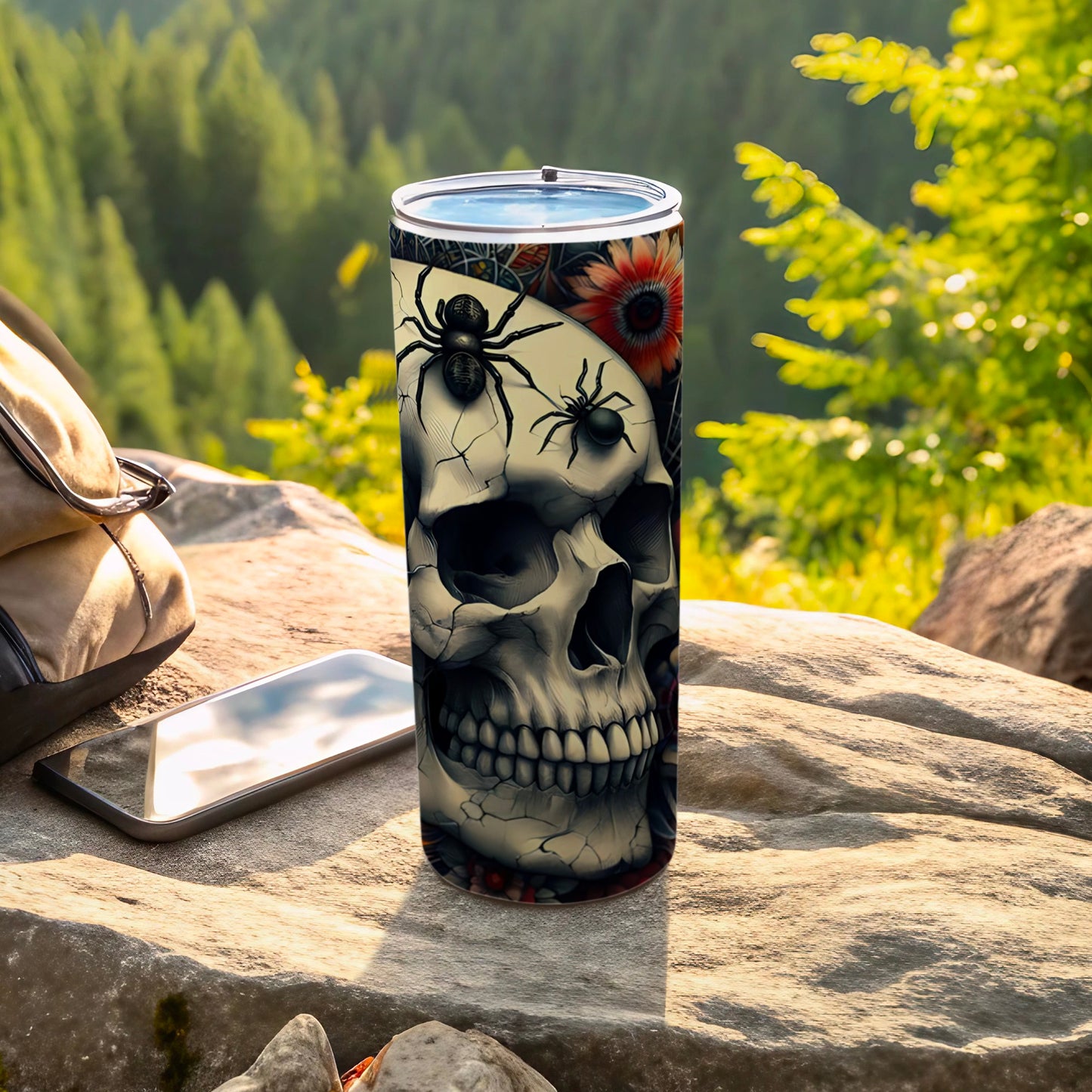 Tumbler with skull, spiders, and floral design on a rock.