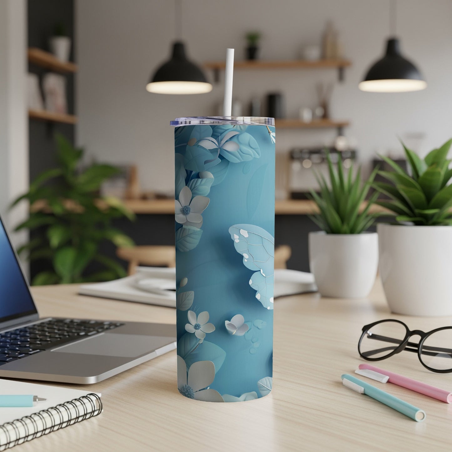 Blue butterfly and floral pattern insulated tumbler with straw on a desk.