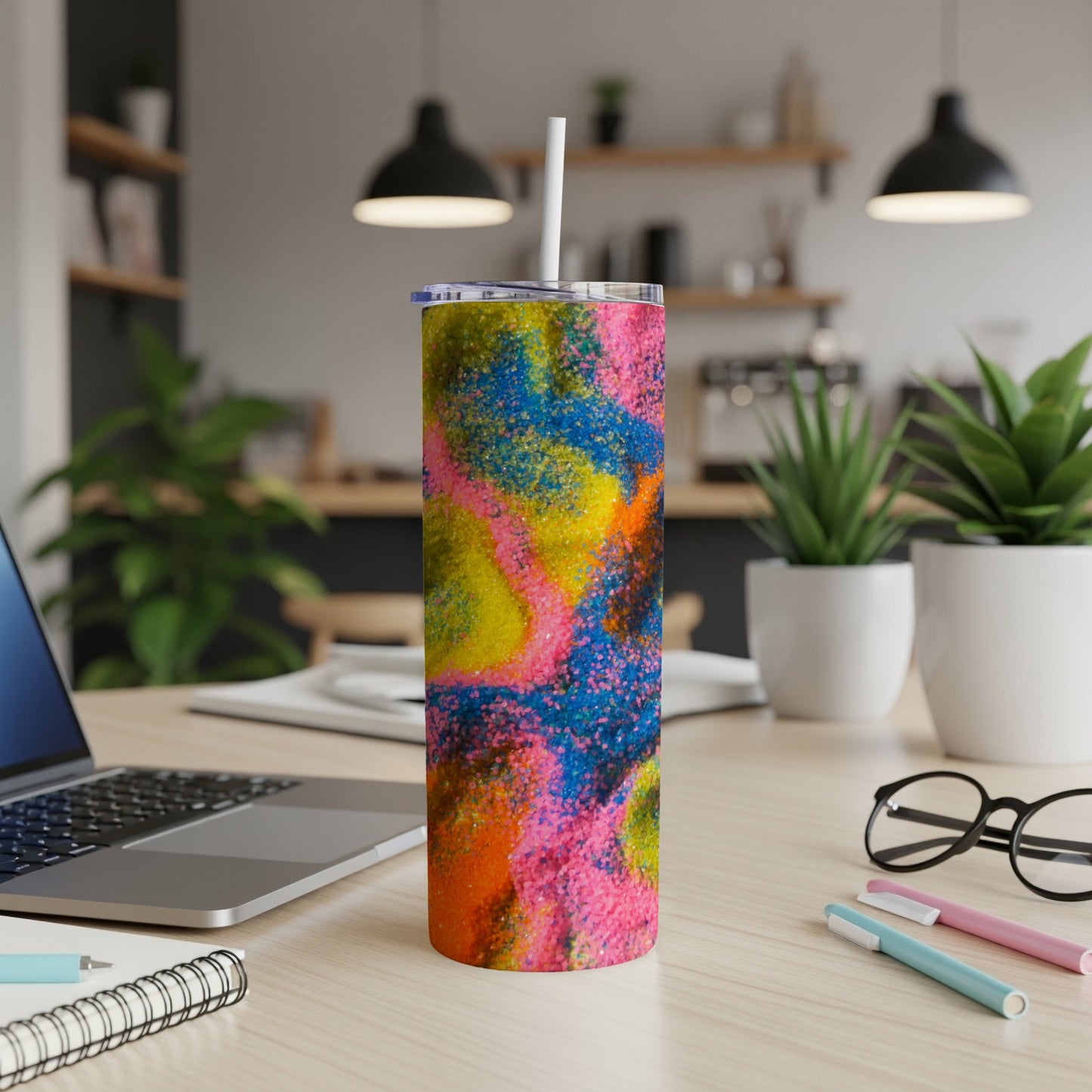 Colorful glitter tumbler with straw on a desk next to a laptop.