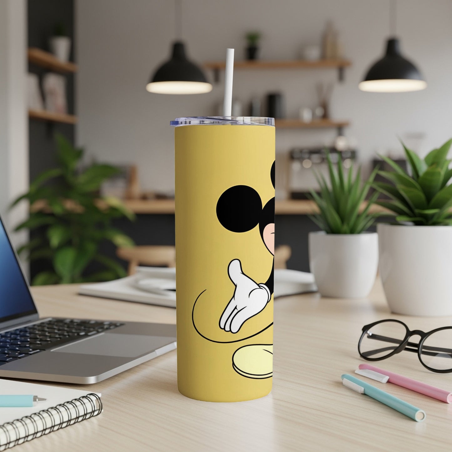Yellow tumbler with Mickey Mouse illustration on a desk with laptop and pens.