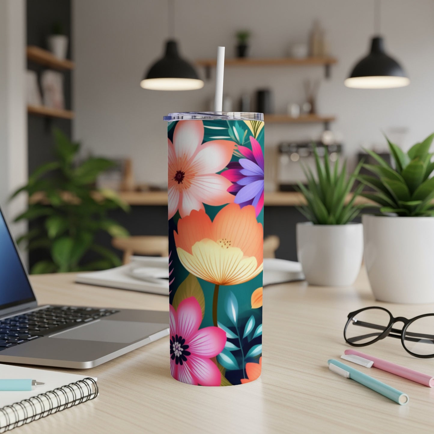 Floral tumbler with straw on desk next to laptop and pens.