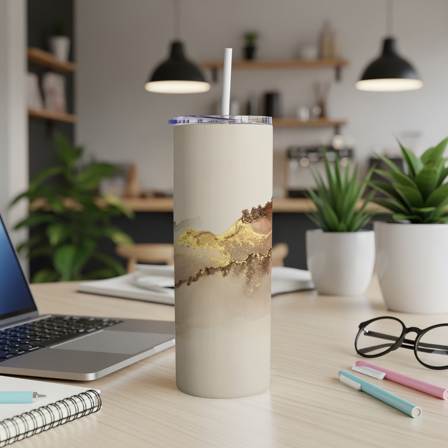 Beige tumbler with gold abstract watercolor design and straw on desk.