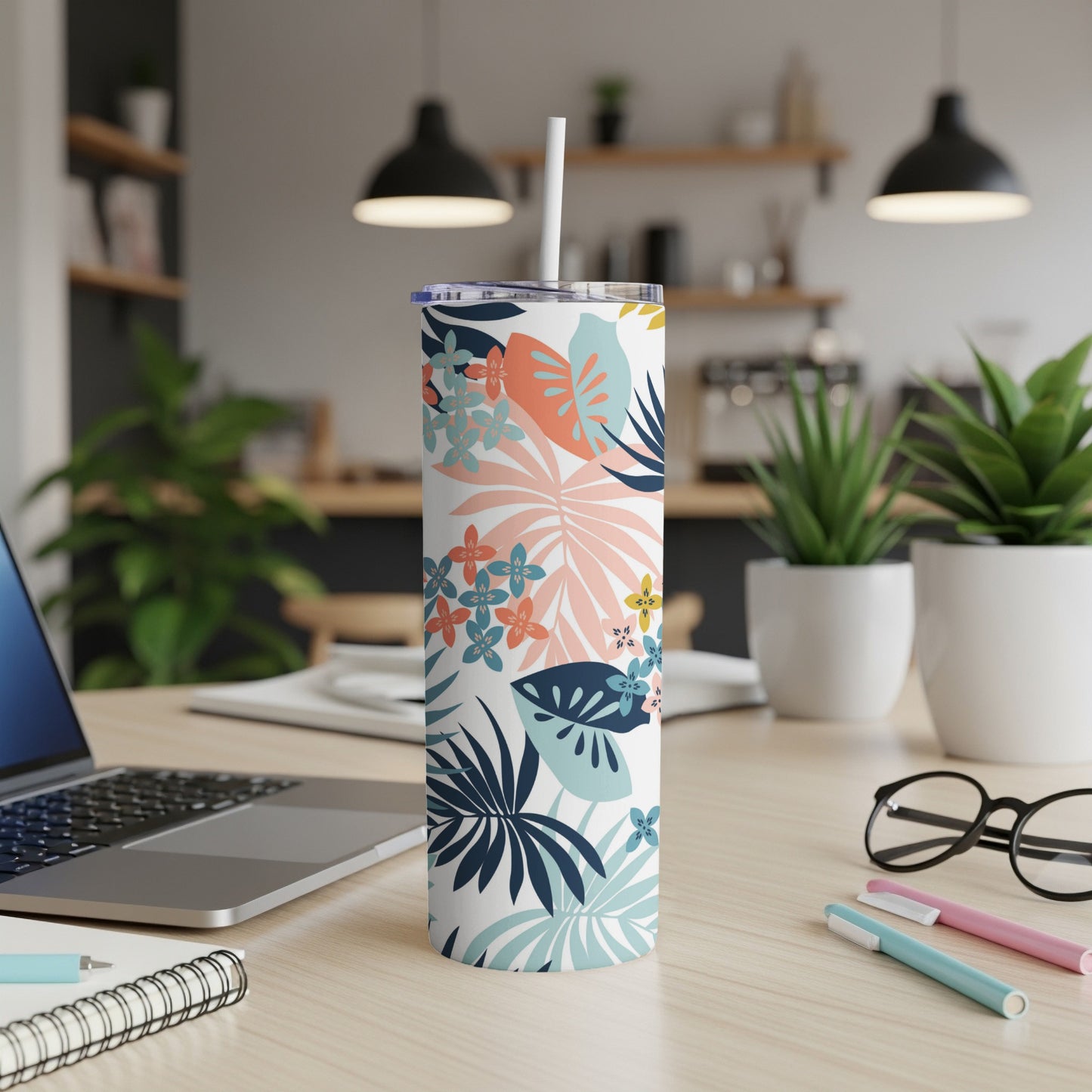 Floral tumbler with straw on desk, laptop and pens in background.