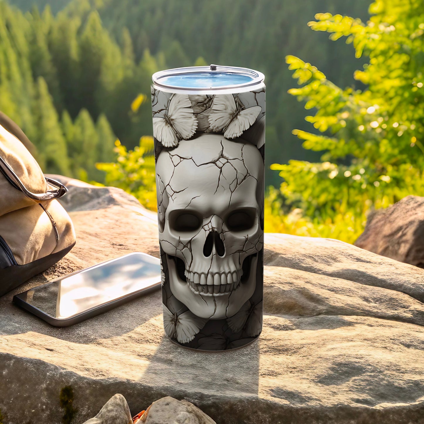 Cracked skull with butterflies design on a tumbler next to a backpack and phone.