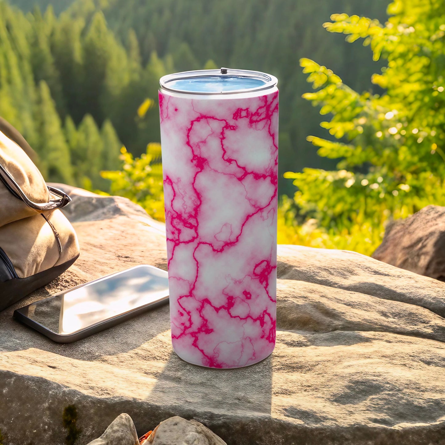 Pink and white marble patterned tumbler on a rock with a phone and backpack.