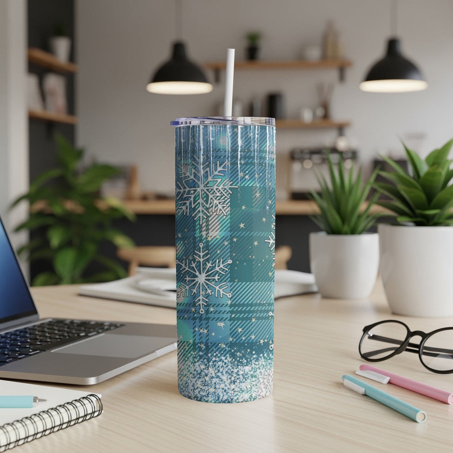Blue plaid tumbler with snowflakes and glitter, on a desk with a laptop.
