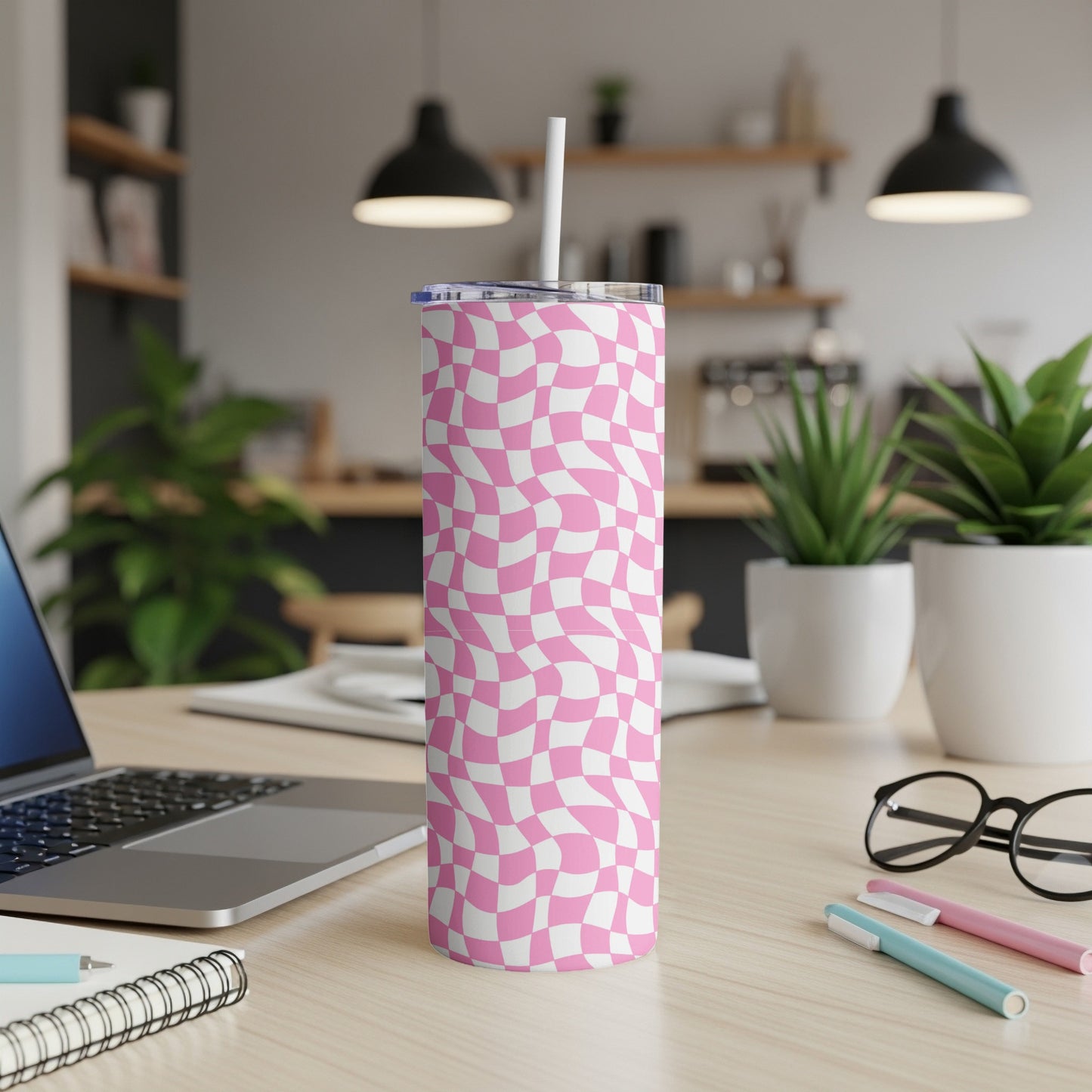 Pink and white checkered tumbler on a desk with a laptop.