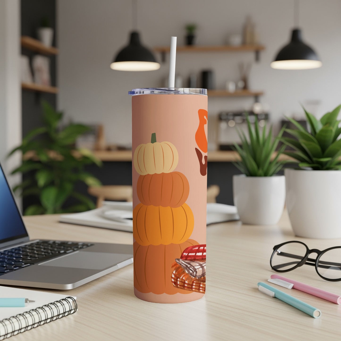 Tumbler with stacked pumpkins and fall leaves on a desk.