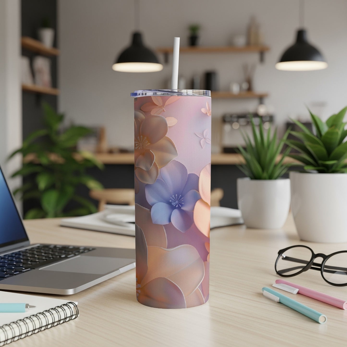 Floral tumbler with straw on desk next to laptop and pens.
