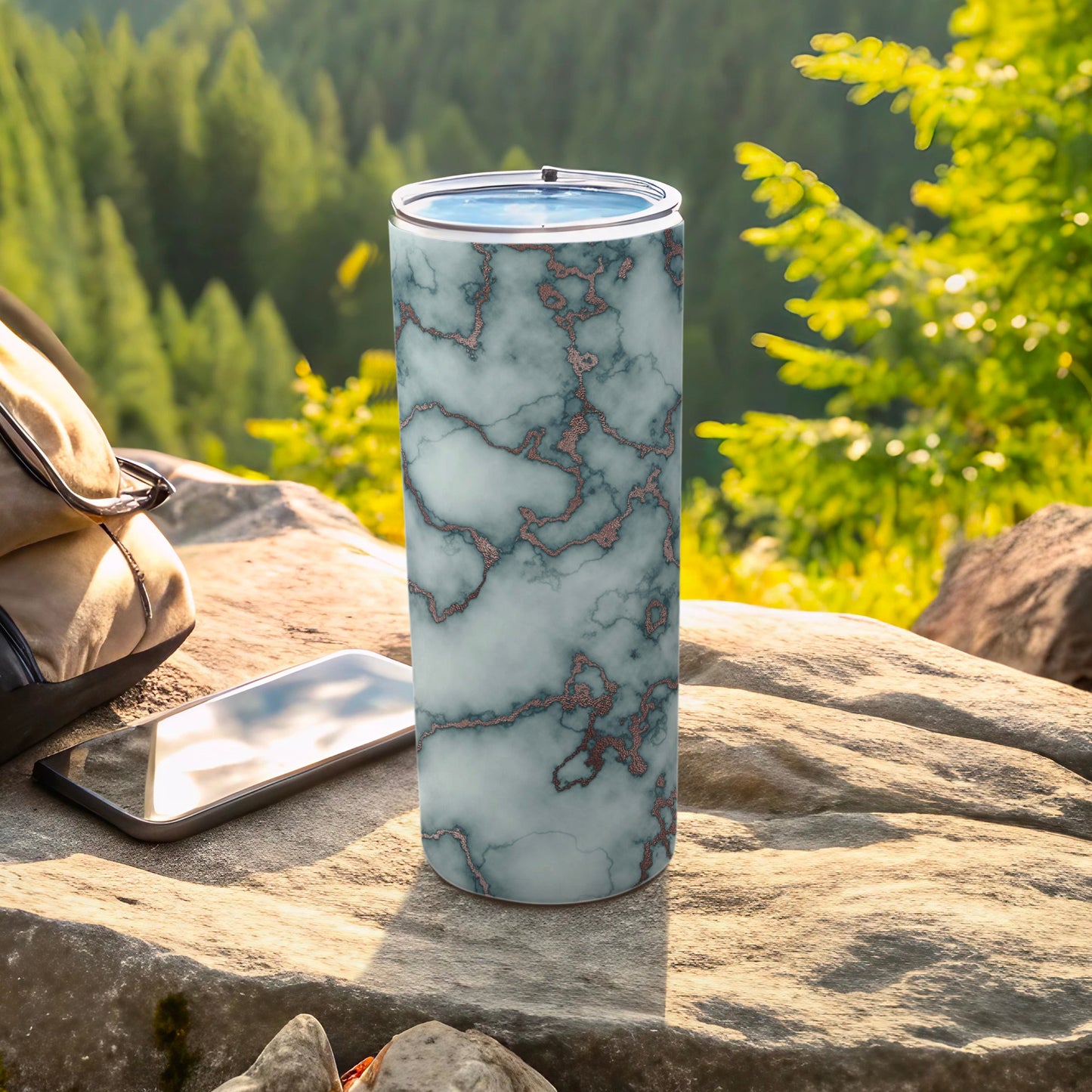 Marble patterned tumbler with rose gold accents outdoors with phone and bag.
