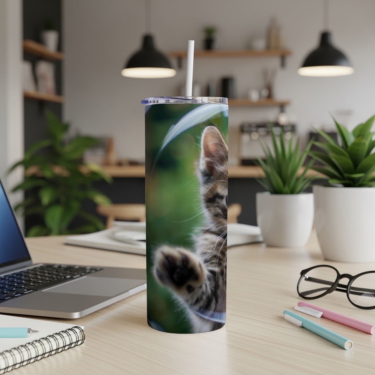 Kitten reaching paw from a blurred green background on a tumbler.