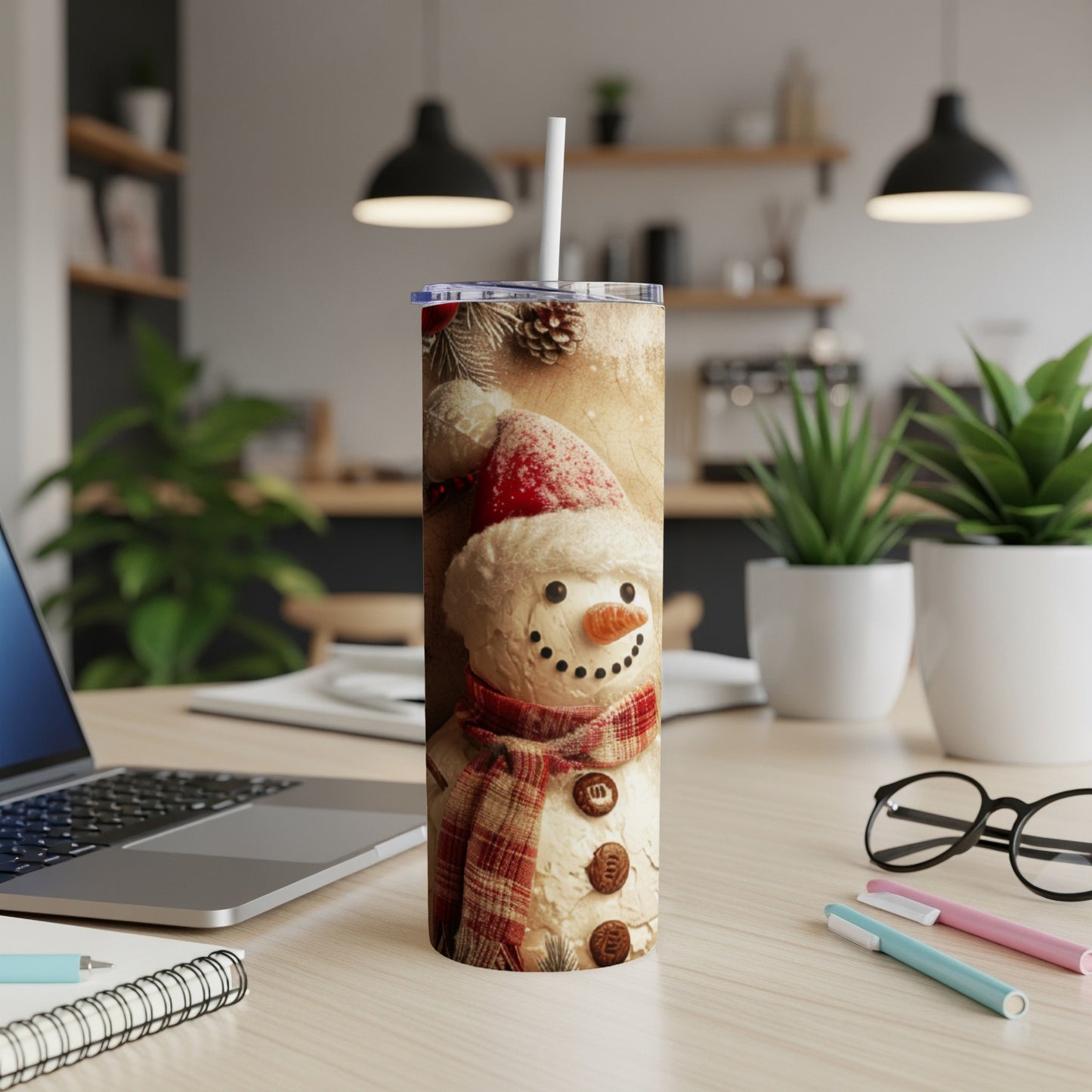 Snowman tumbler with red scarf and Santa hat, on a desk with laptop.
