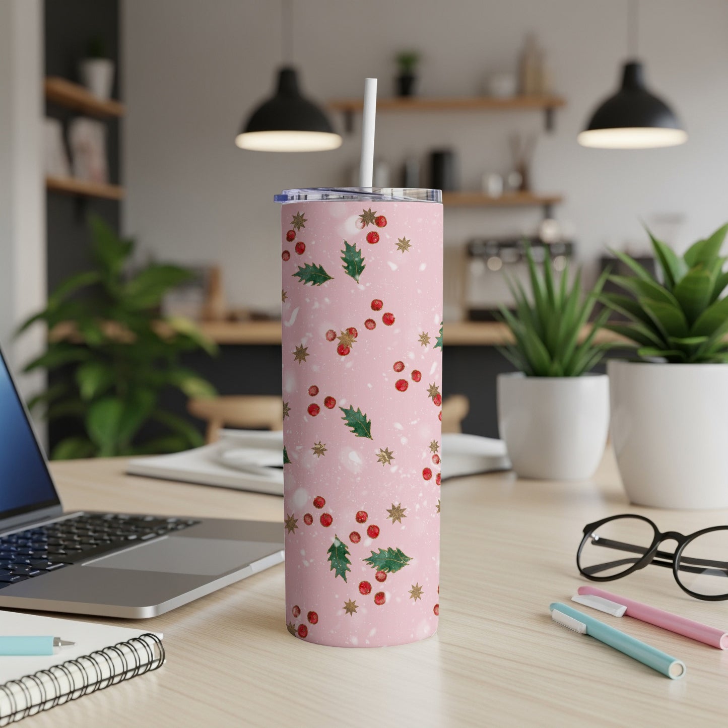 Pink tumbler with holly and berry pattern, white straw, on a desk.