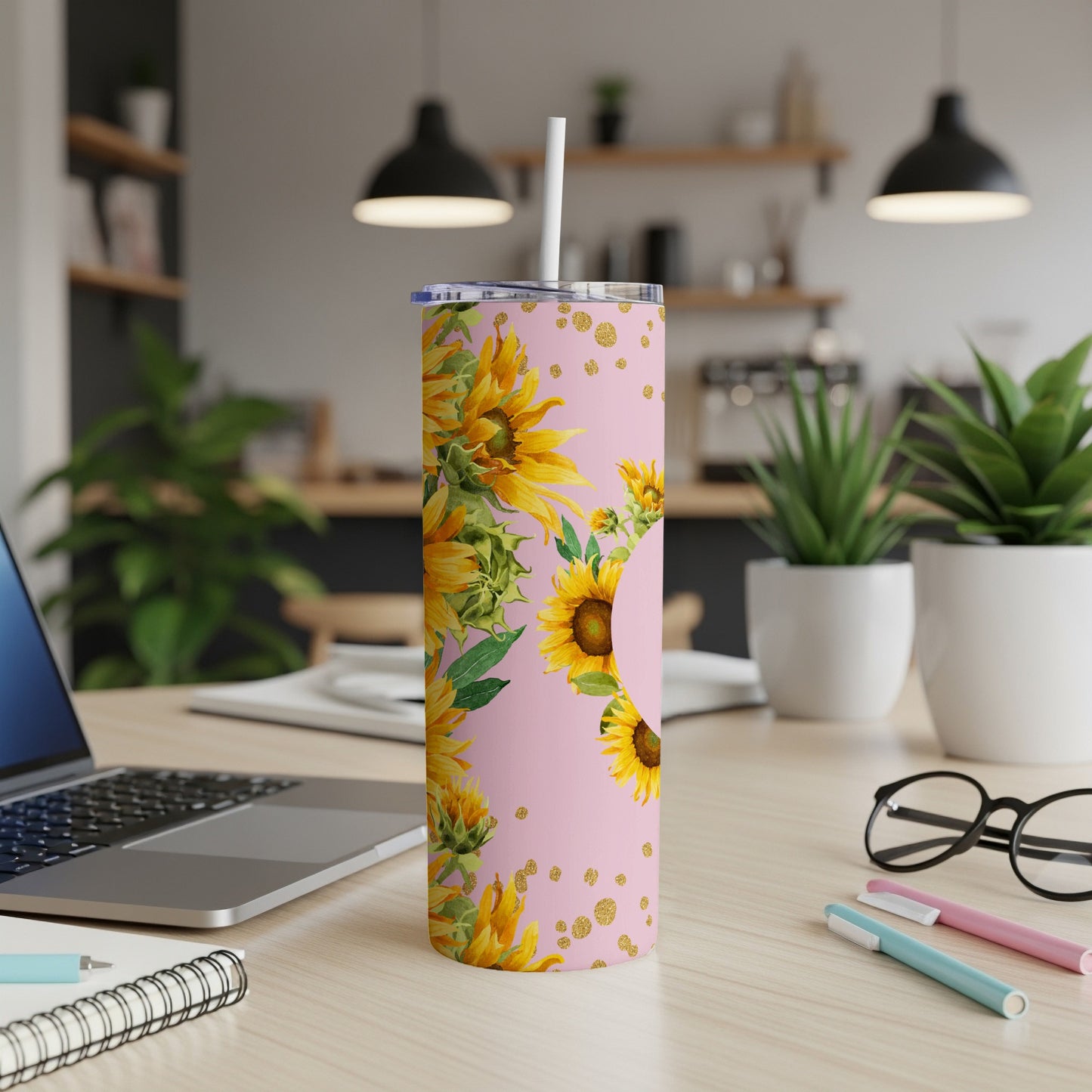 Pink tumbler with sunflowers and gold glitter accents on a desk.