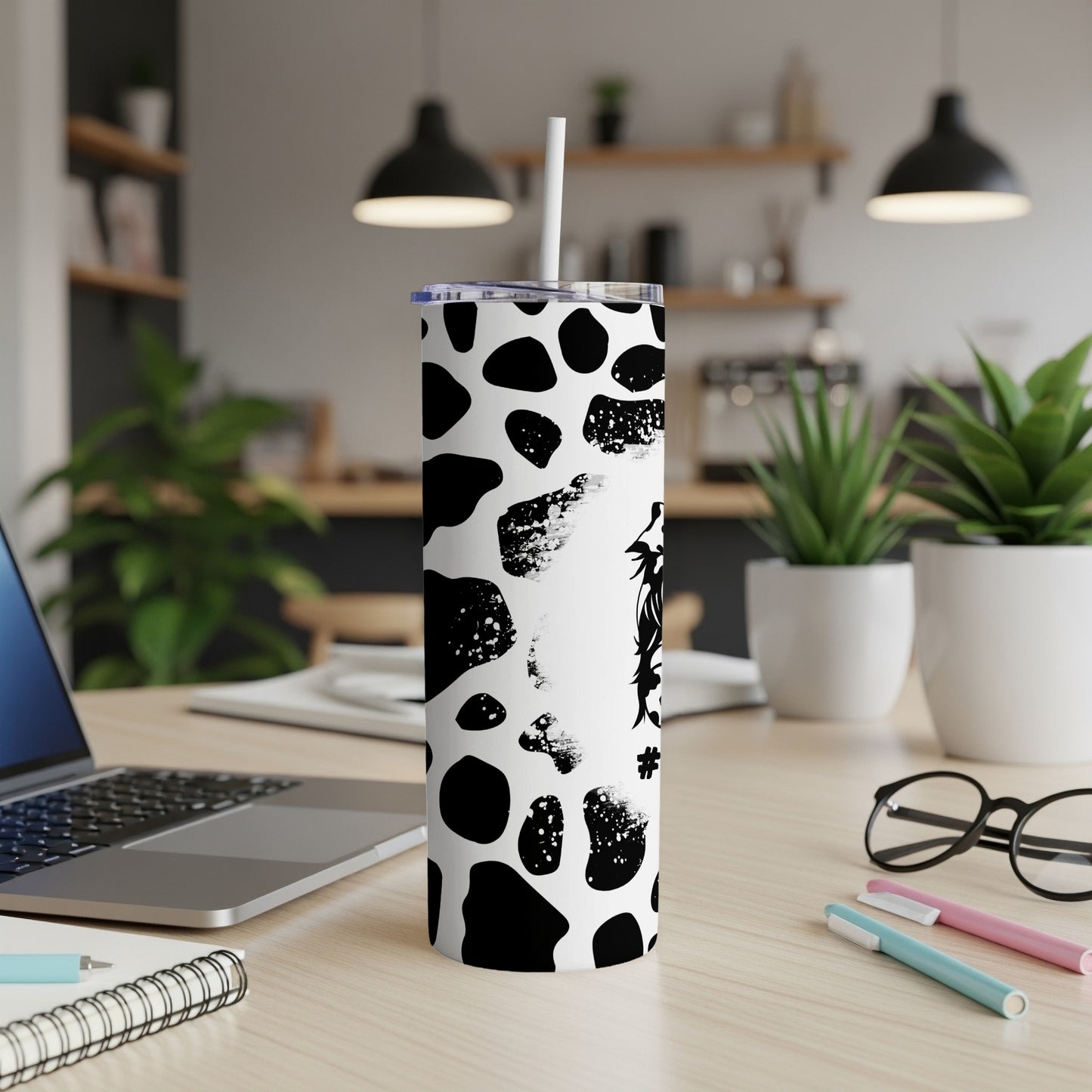 White tumbler with black cow print pattern and straw on a desk.