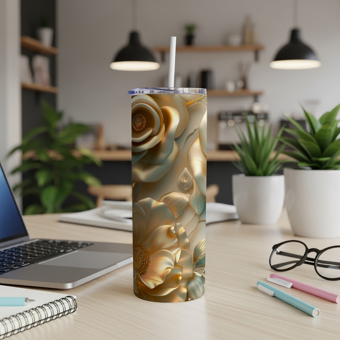 Gold floral print tumbler with straw on a desk beside a laptop.