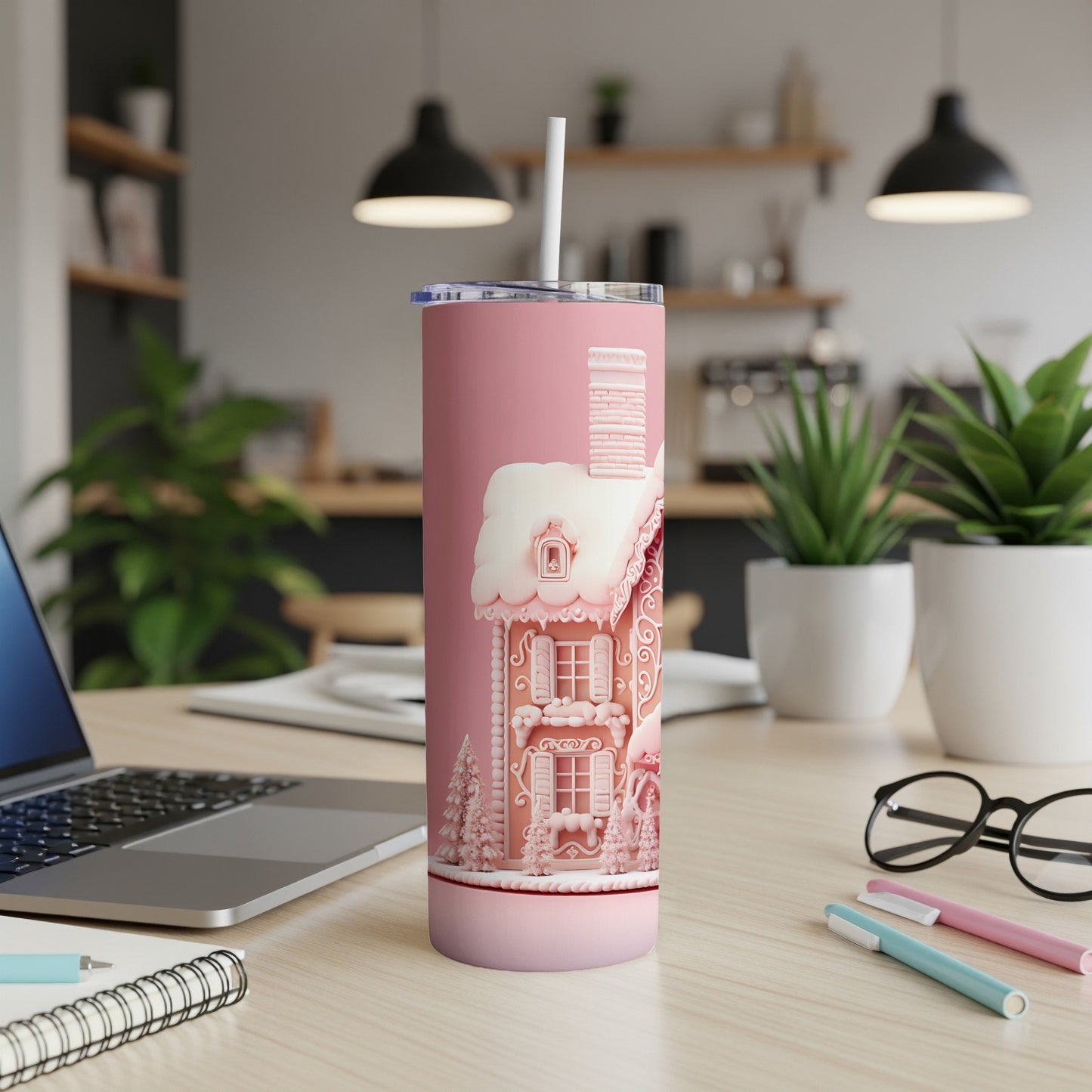 Pink tumbler with a gingerbread house design and white straw on a wooden desk.