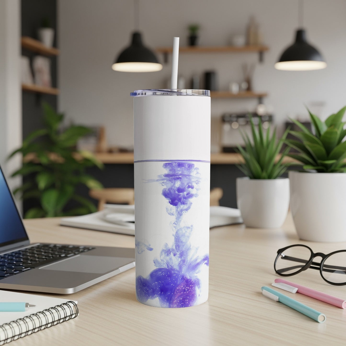 White tumbler with purple ink swirl design, on a desk with laptop and pens.