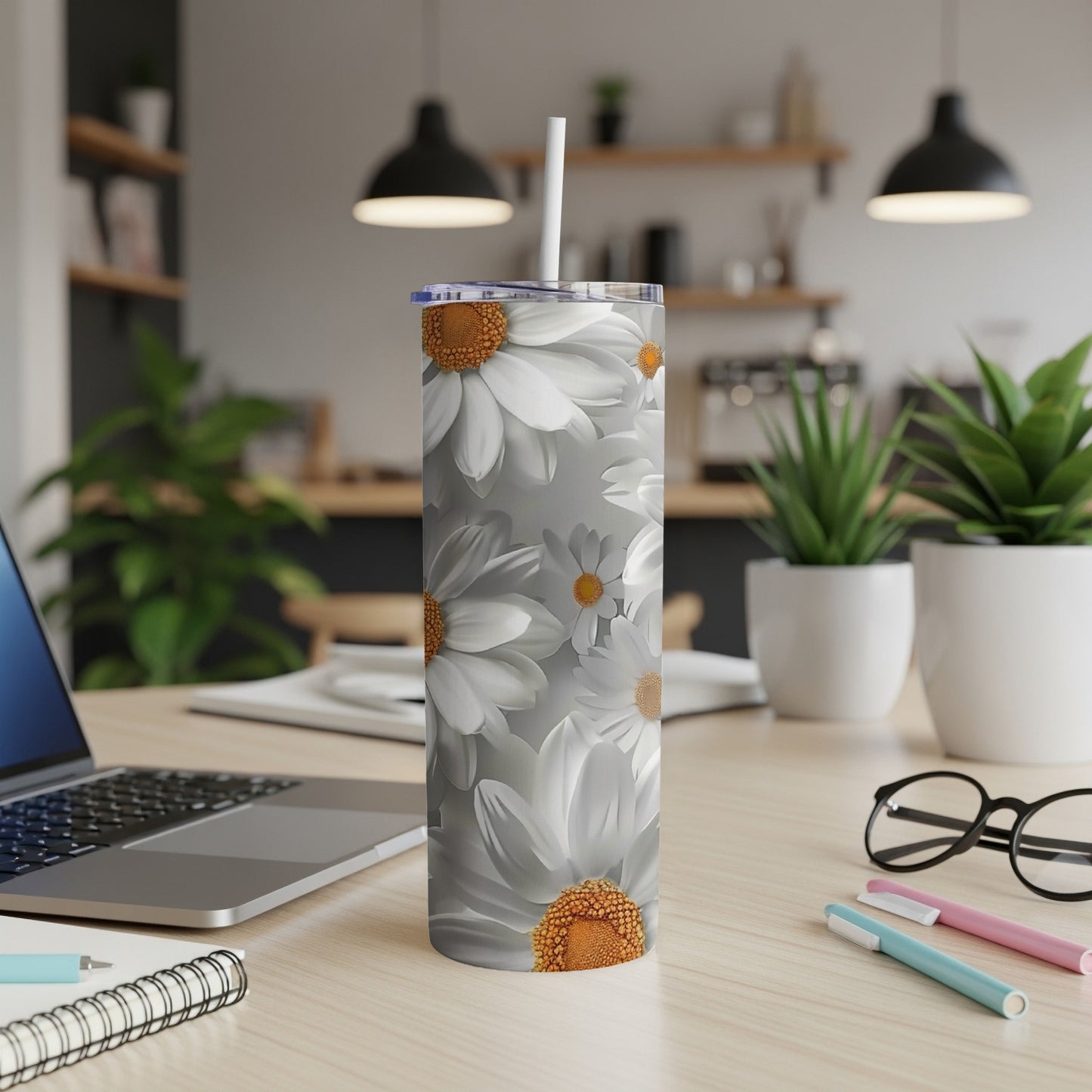 Silver tumbler with a white daisy pattern on a desk with a laptop.
