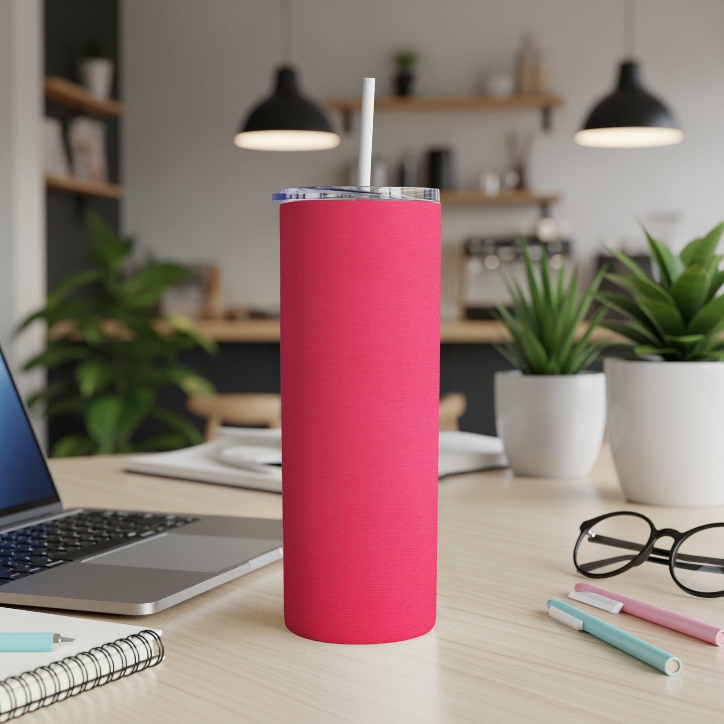 Pink tumbler with straw on a wooden desk with laptop and pens.