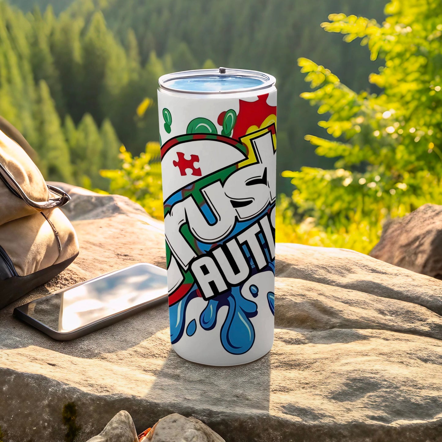 White tumbler with "Just Autism" text and puzzle pieces, beside a phone and backpack.