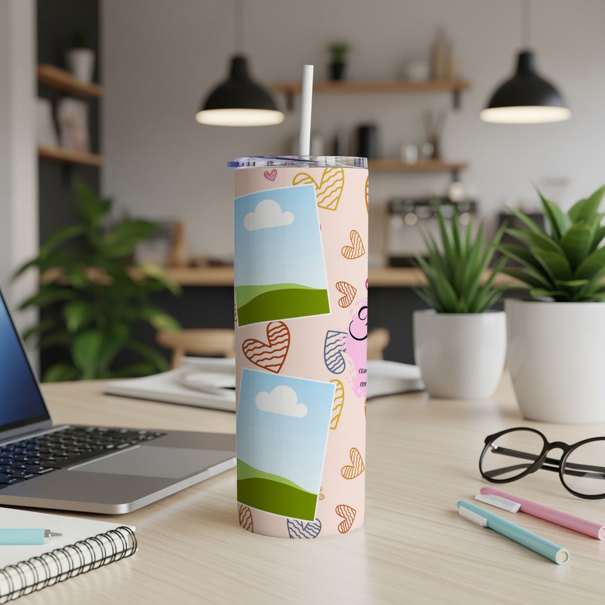 Pink tumbler with cartoon hearts, photo frames, and a straw on a desk.