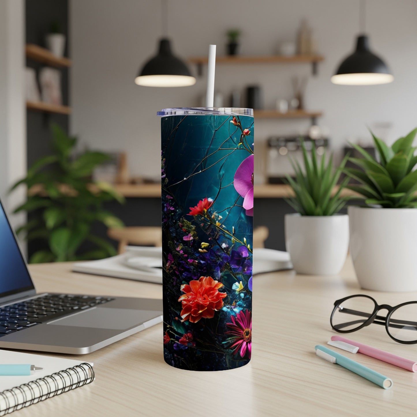 Tall tumbler with dark floral pattern on desk with laptop and pens.