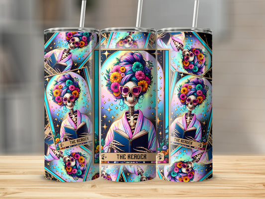 Skeleton reading a book with colorful flowers and stars on a patterned tumbler.