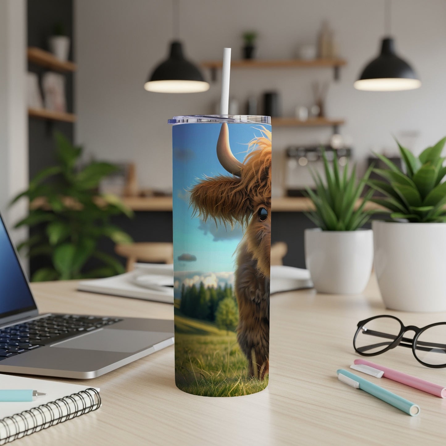 Highland cow illustration on a tumbler, with laptop and pens on desk.