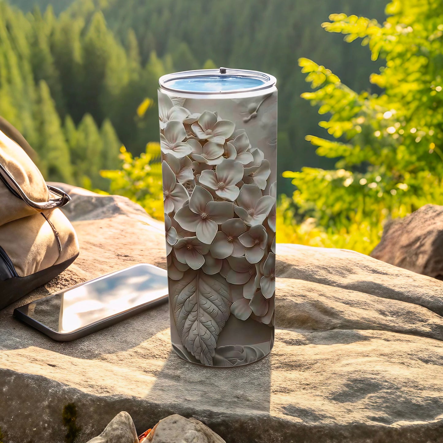 Gray floral tumbler next to a smartphone and backpack on a rock.