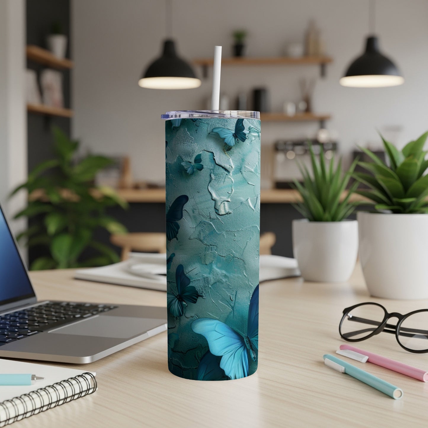 Teal skinny tumbler with blue butterfly design on a desk.