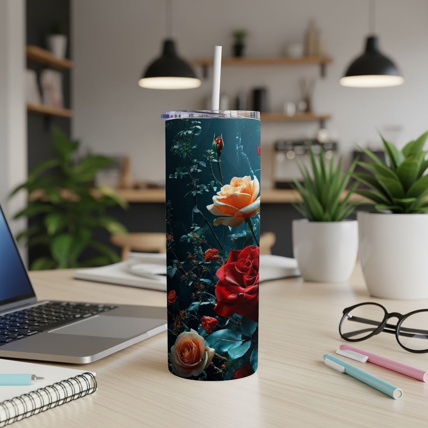 Floral tumbler with roses and leaves on a desk with laptop and pens.