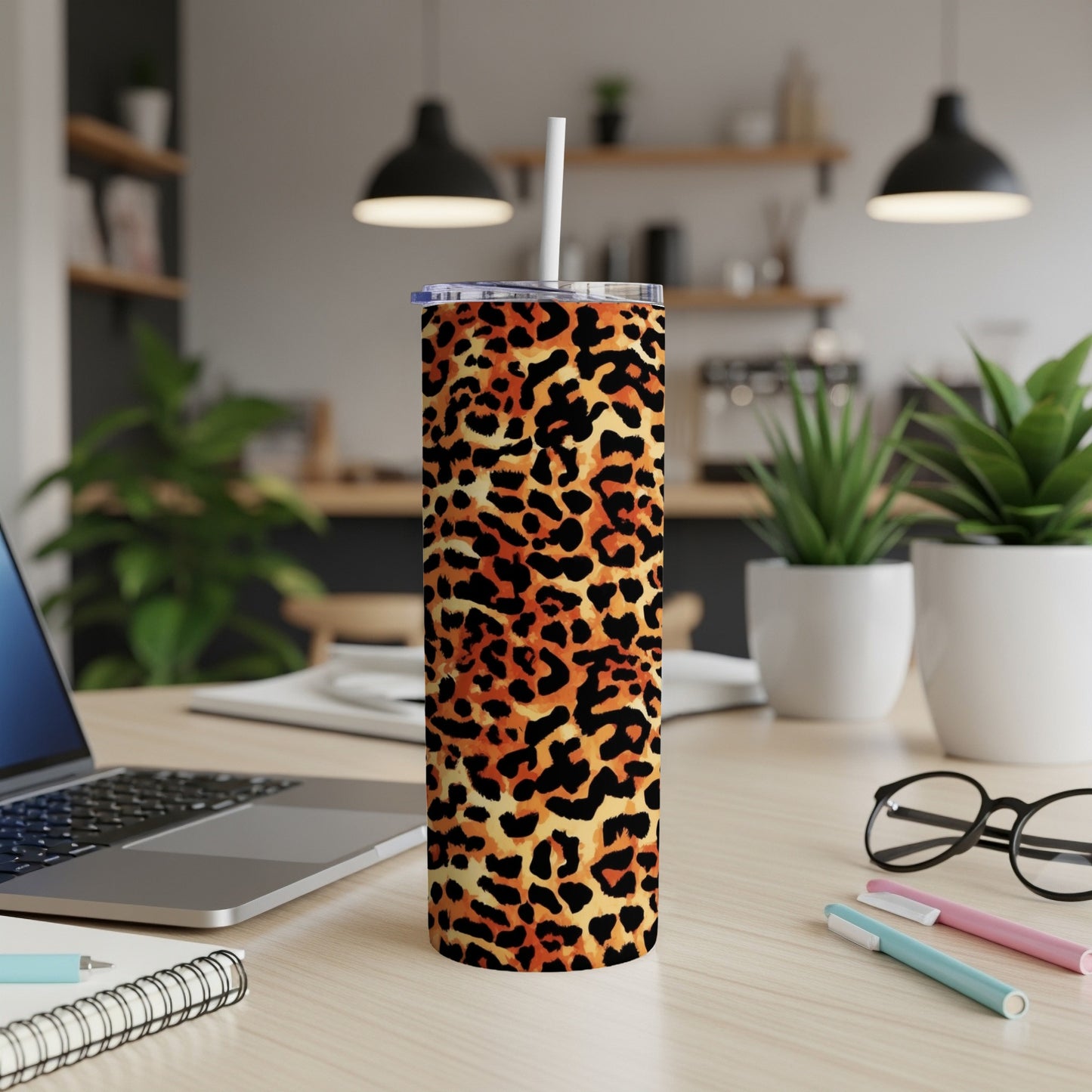 Leopard print tumbler with a straw on a desk next to a laptop.