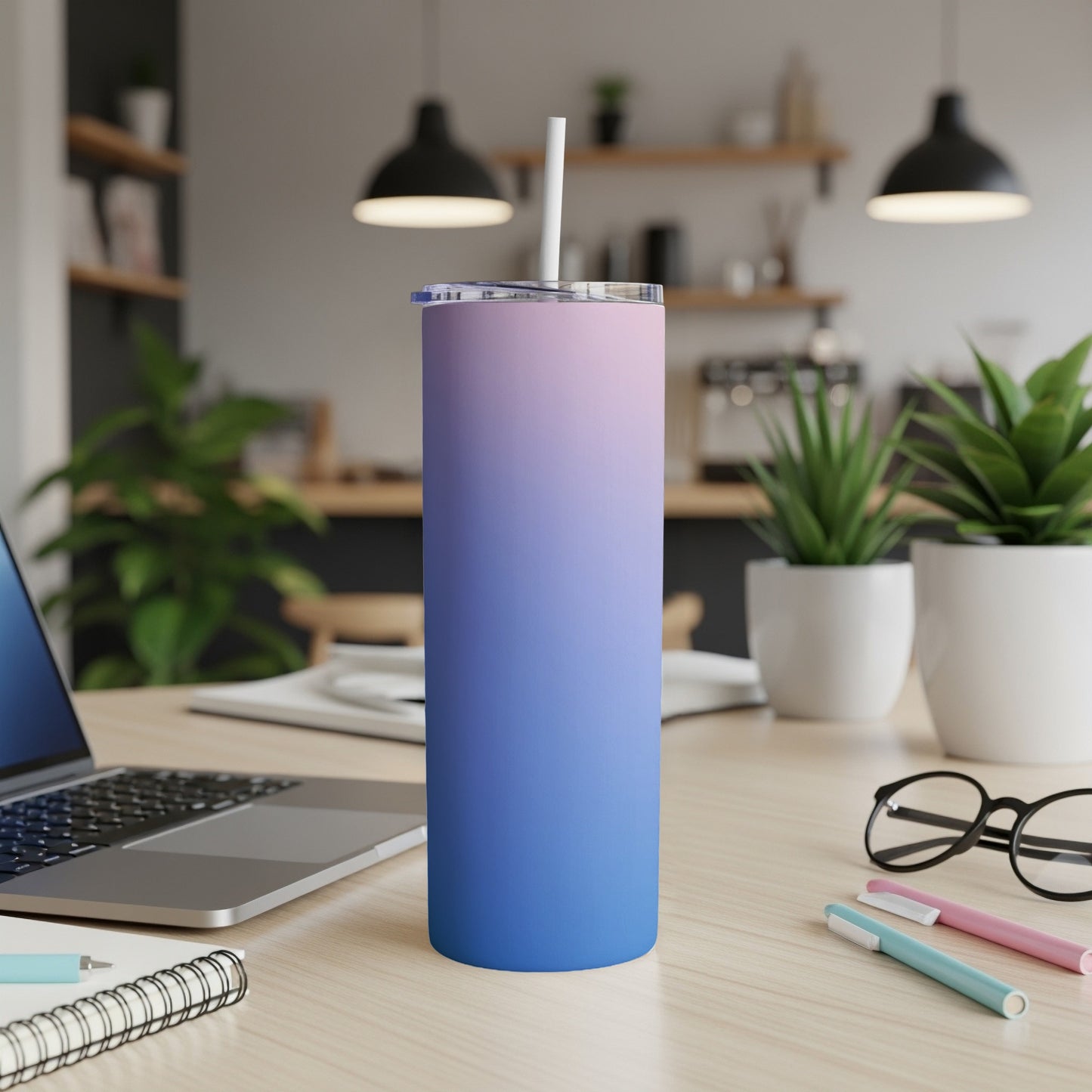 Gradient pink and blue skinny tumbler with a straw on a desk.