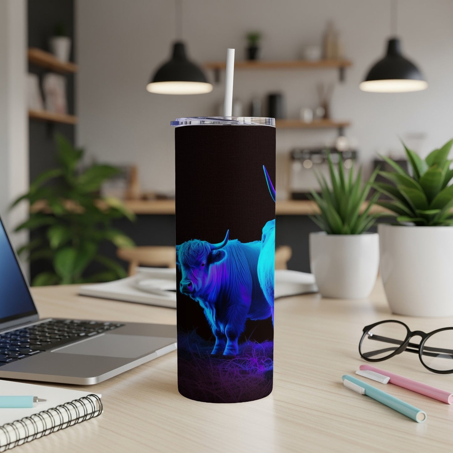 Black tumbler with a neon blue highland cow design on a desk.