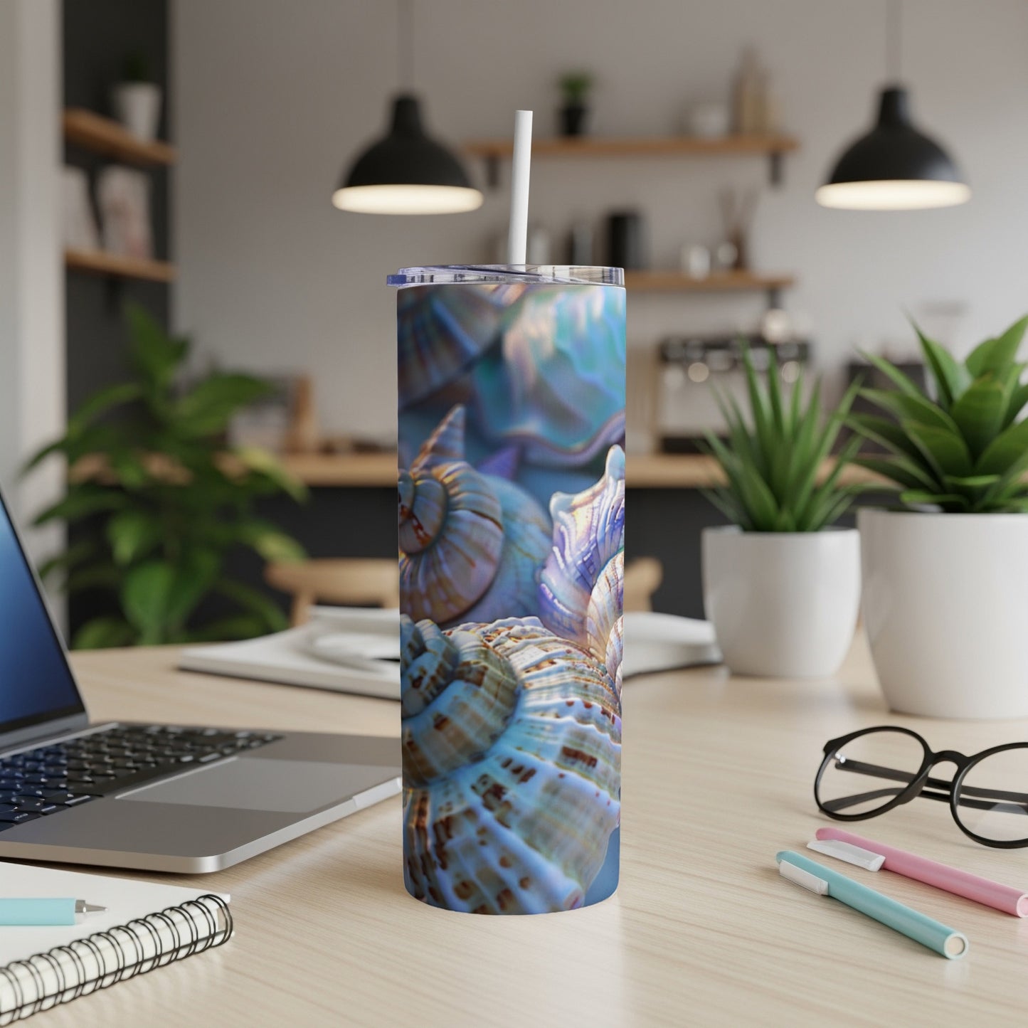 Blue and purple seashells cover a tumbler on a desk with a laptop.