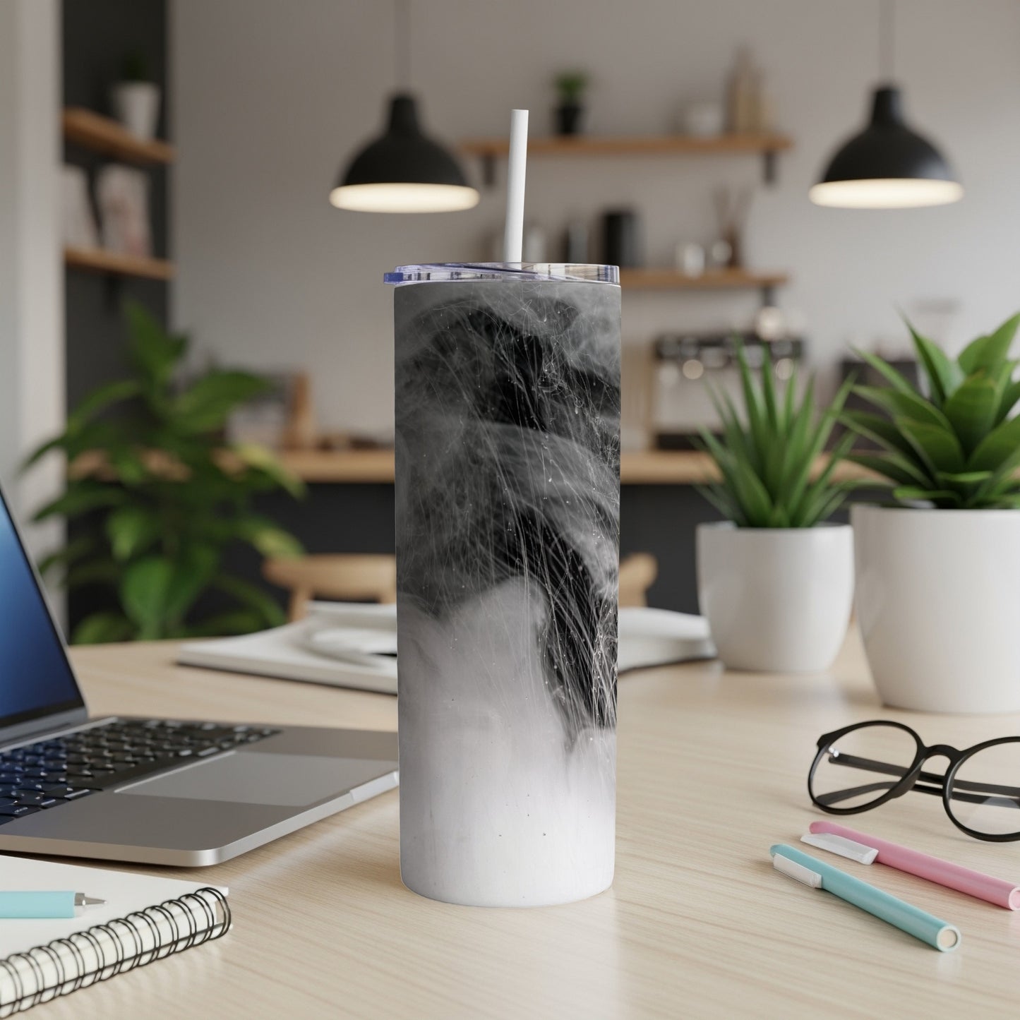 White tumbler with black abstract smoky design, straw, on desk.