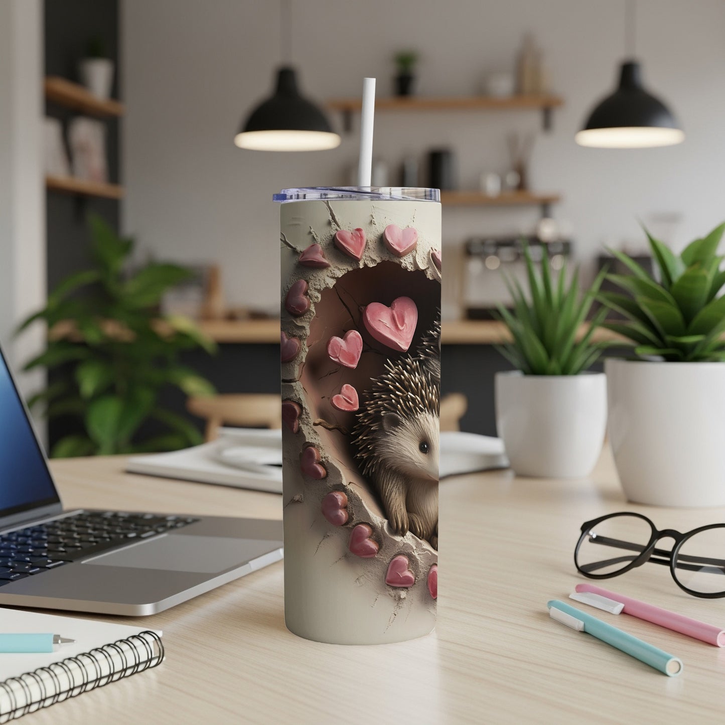 Cream tumbler with hedgehog and heart-shaped cutouts, laptop and pens nearby.