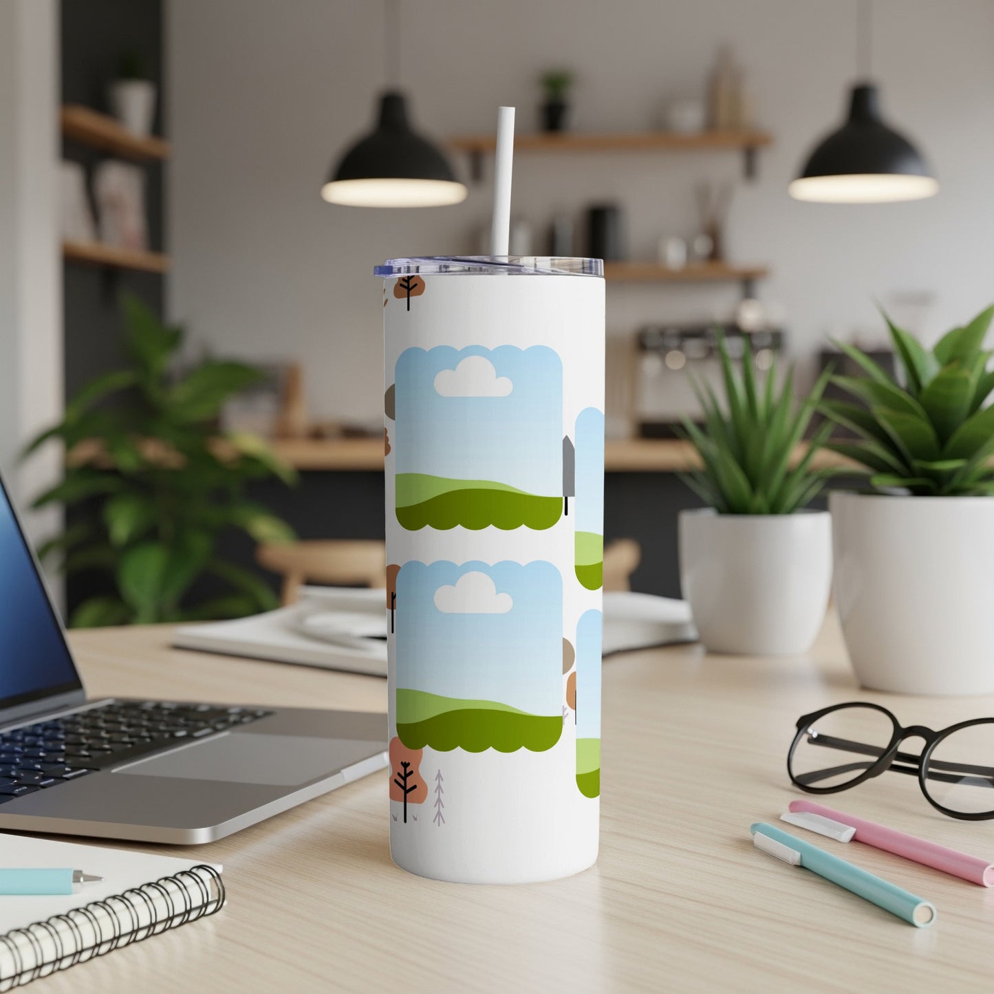 White tumbler with a whimsical landscape design and straw on a wooden desk.