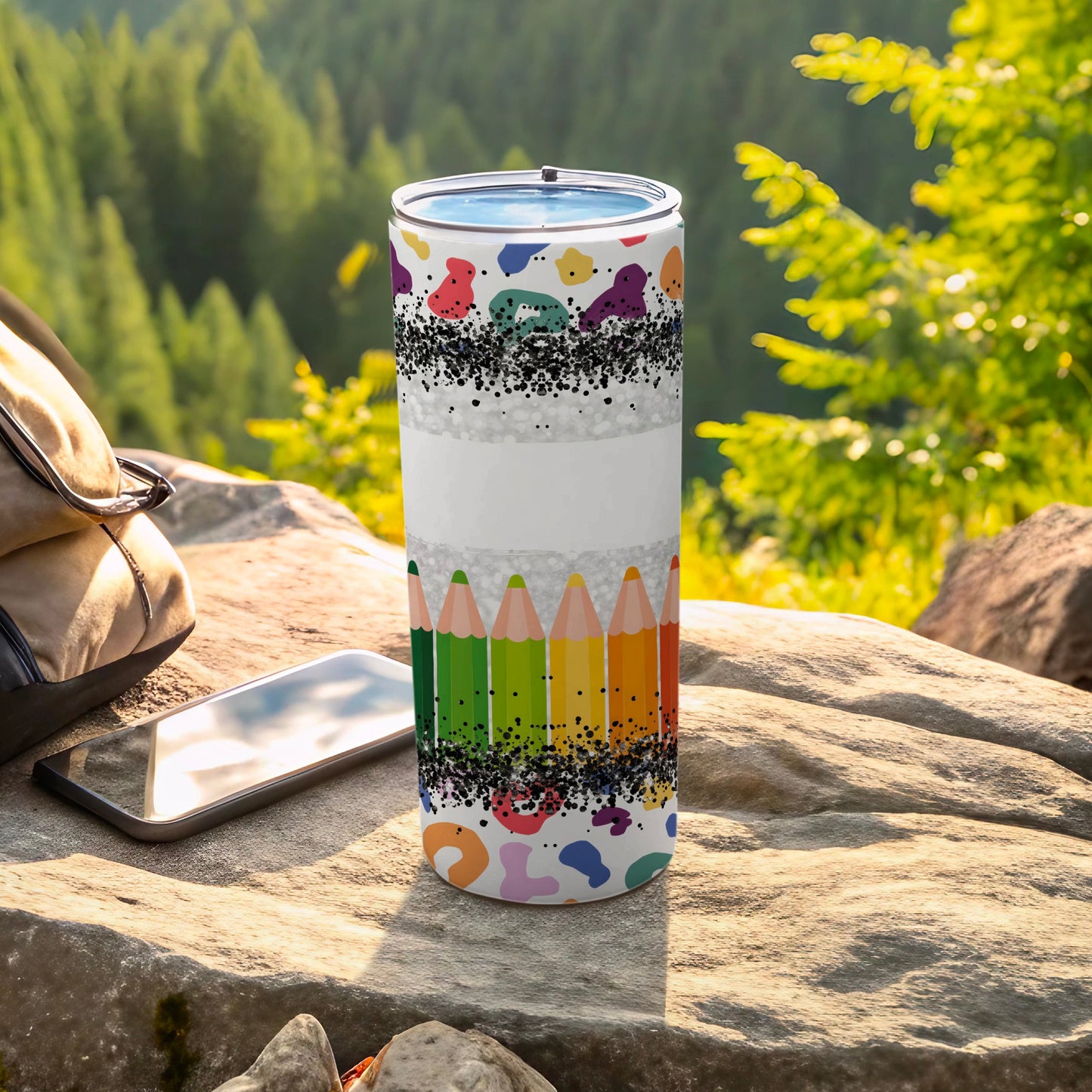 Tumbler with colorful crayon and confetti pattern on a rock with a backpack.