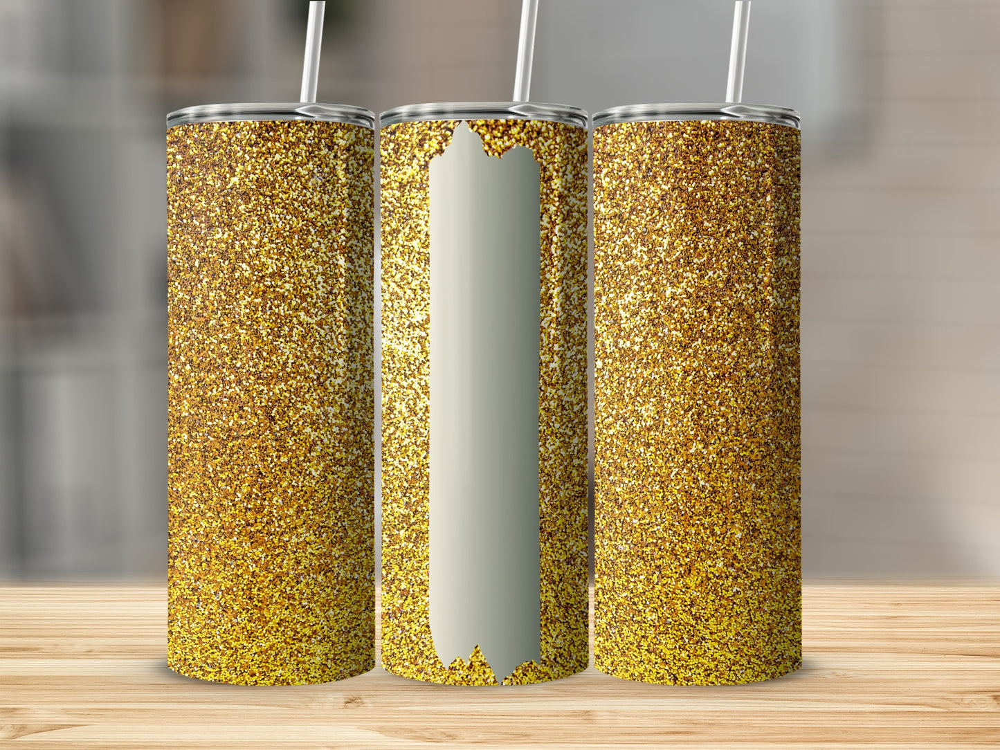 Three glittery gold tumblers with white straws on a wooden surface.