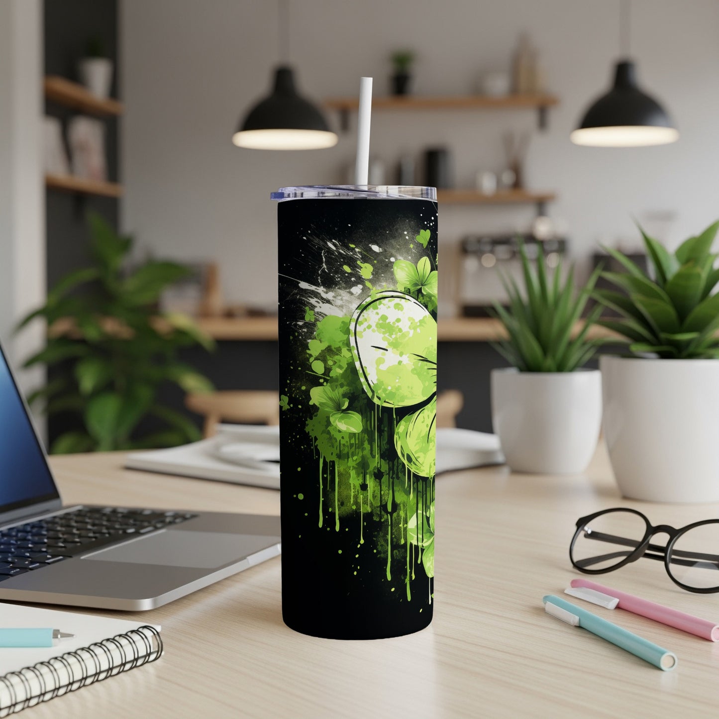 Black tumbler with green splatters and shamrock design, standing on a desk.