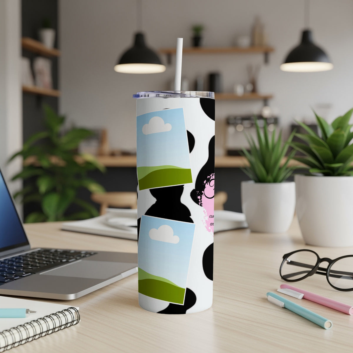 Cow print tumbler with sky and grass graphics and a cartoon face.