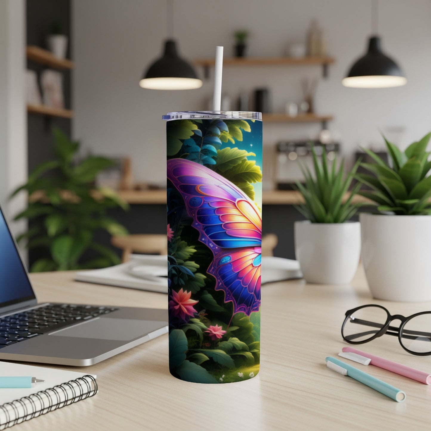 Butterfly wing design on a tall tumbler, with plants and a laptop in background.