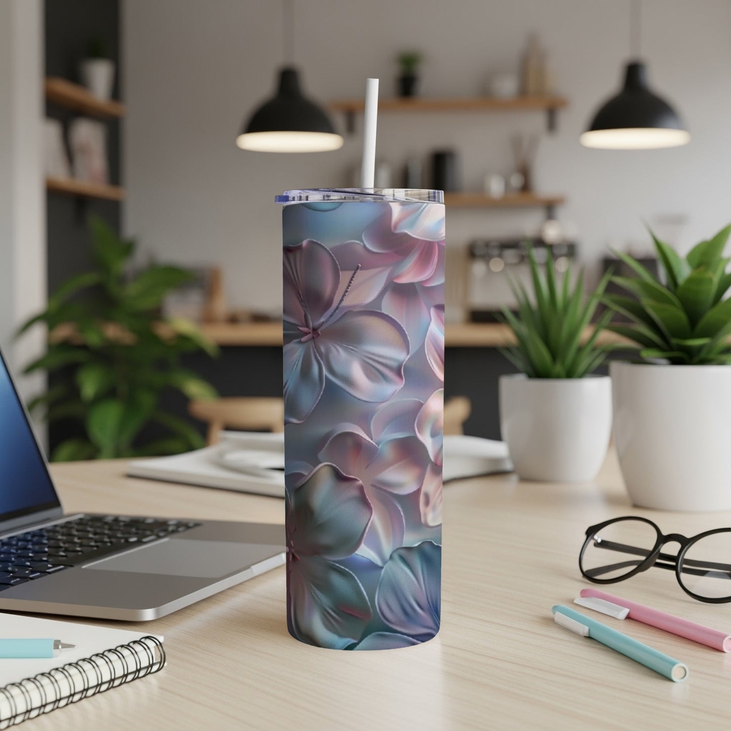 Floral patterned tumbler with straw on a desk with a laptop and pens.