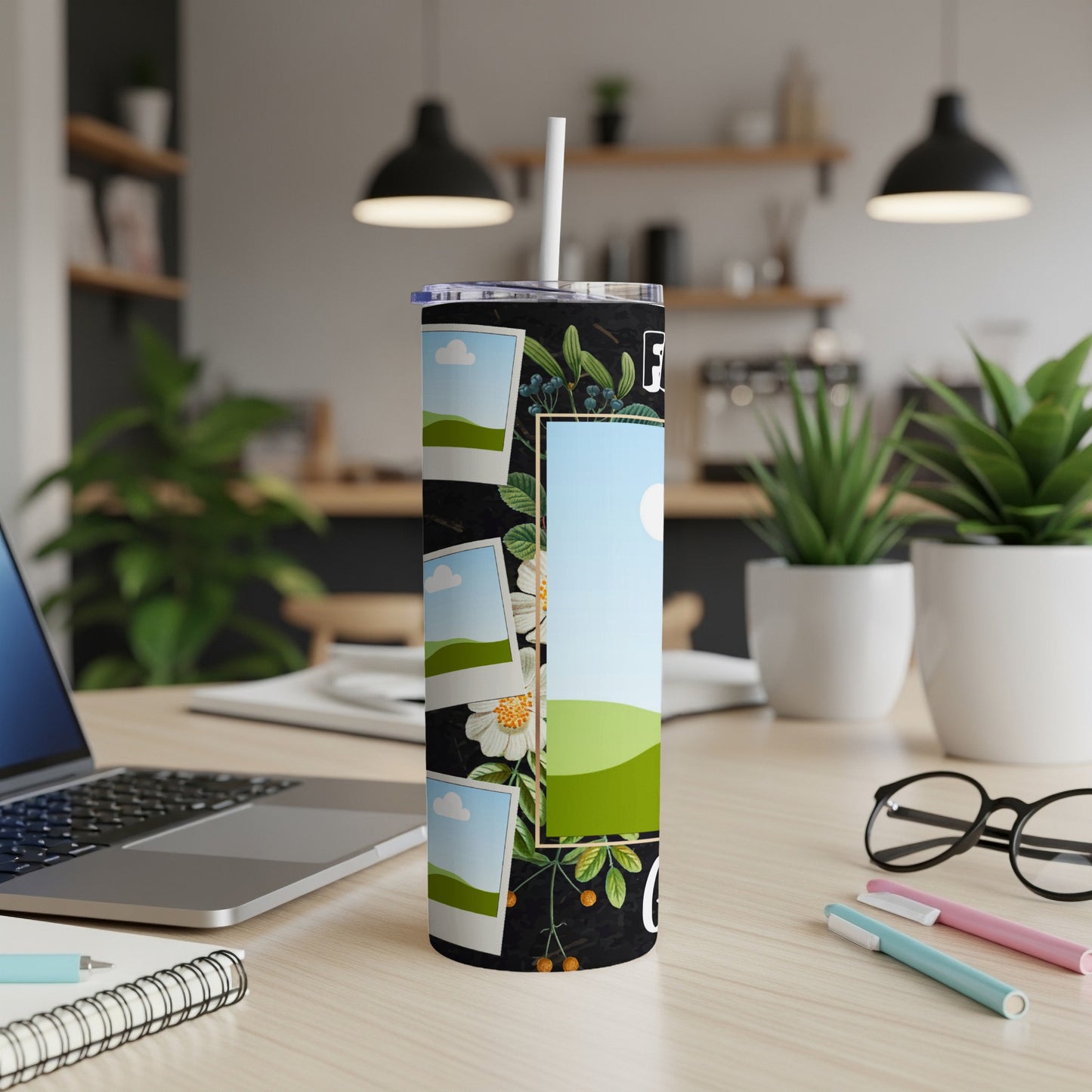 Black tumbler with floral design and photo frames on a desk with laptop and glasses.